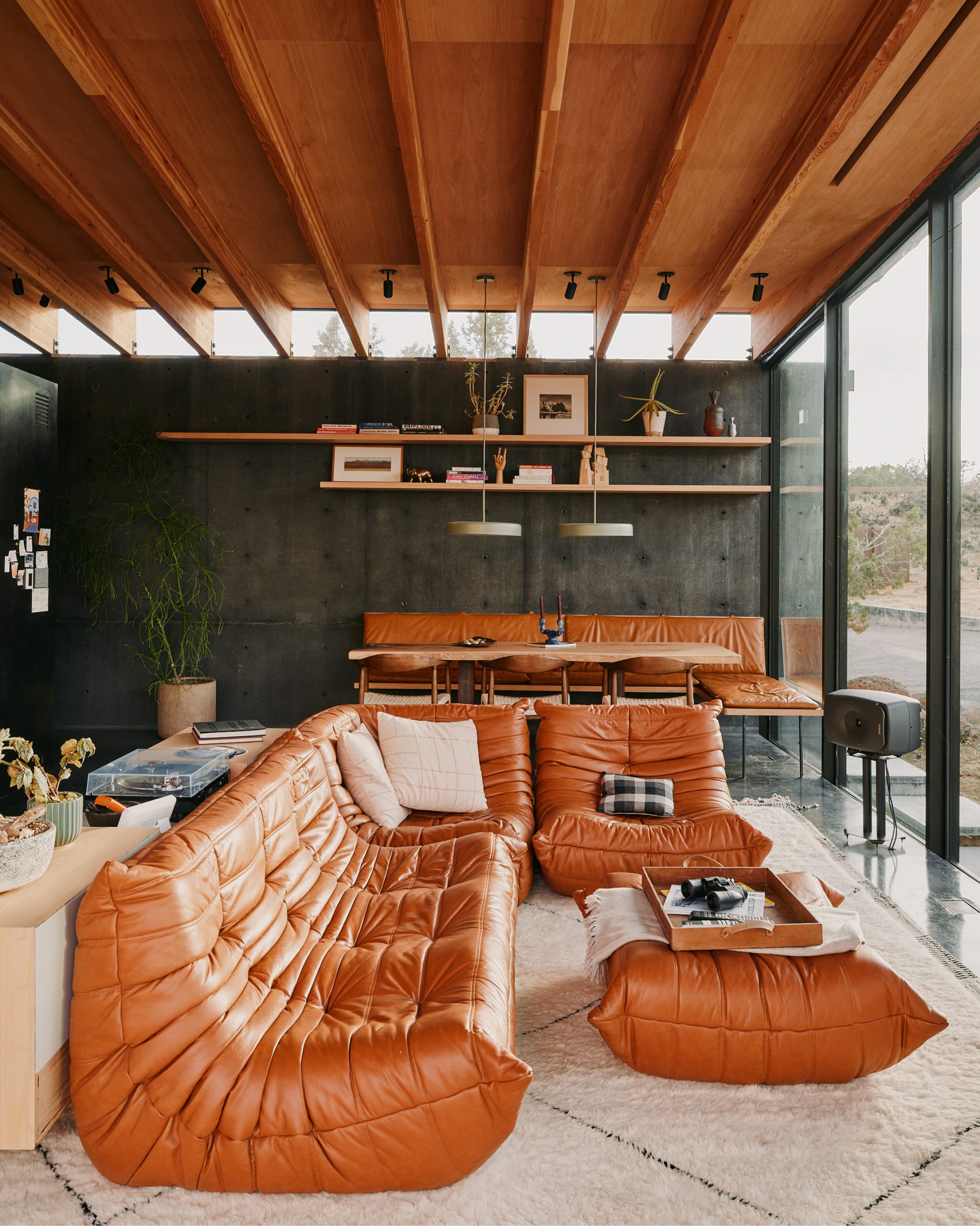 A cognac leather Togo sofa on a wool rug, board-formed concrete walls, timber ceiling, desert beyond the glass.