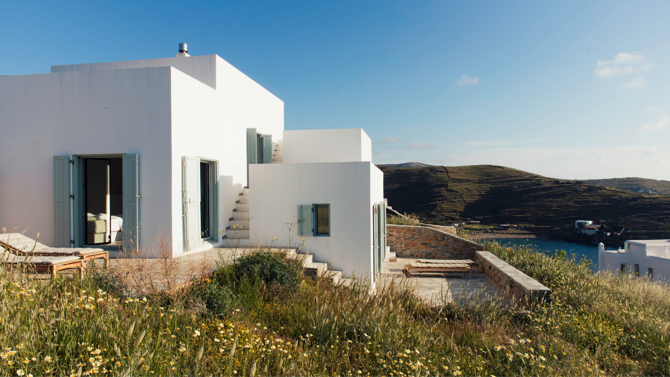 Piperi House — a whitewashed Cycladic house with pale sage shutters above a blue Aegean bay on Kythnos.